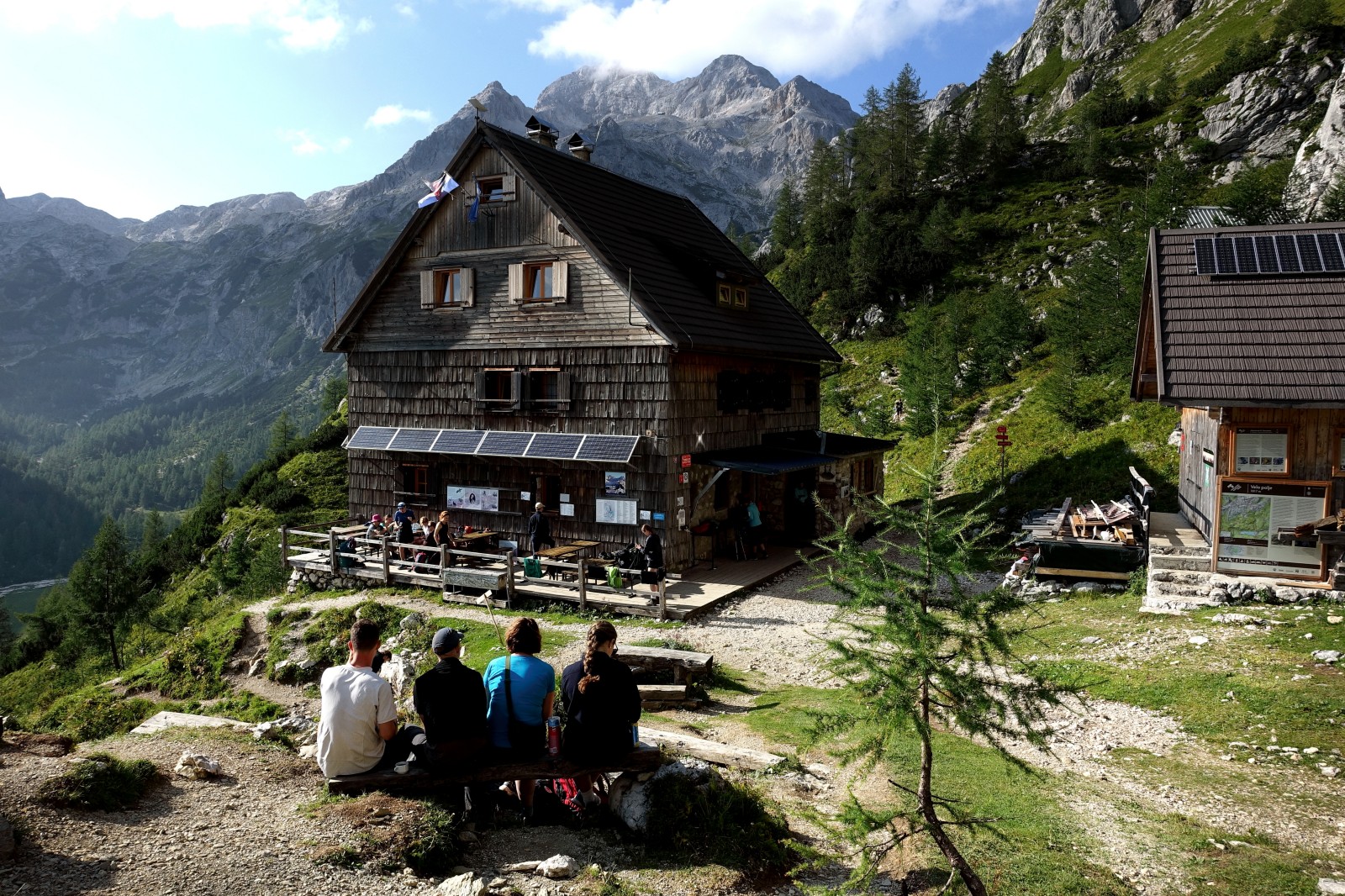 Pohodniki med pocitkom pred Vodnikovim domom na Velem polju (1820 m), v ozadju Triglav.